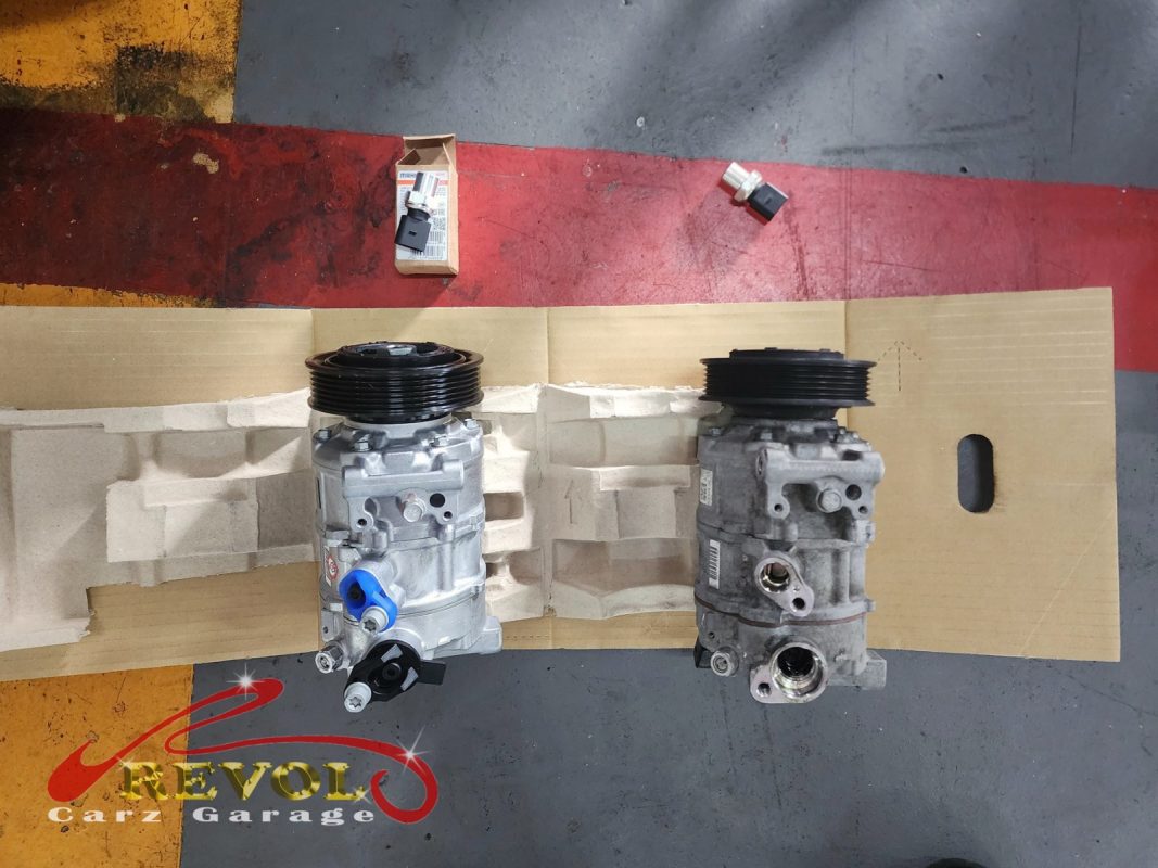 The old AC compressor removed beside the new Audi-spec replacement and receiver-drier.