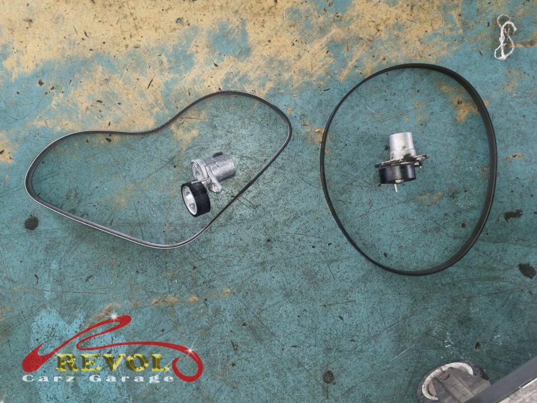 The auxiliary belt, tensioner and idler pulley laid out. On an accessory drive these are replaced as a set, not one at a time.