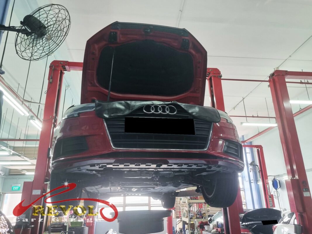 The red Audi A3 up on the two-post lift, fender cover on, in for its scheduled service.