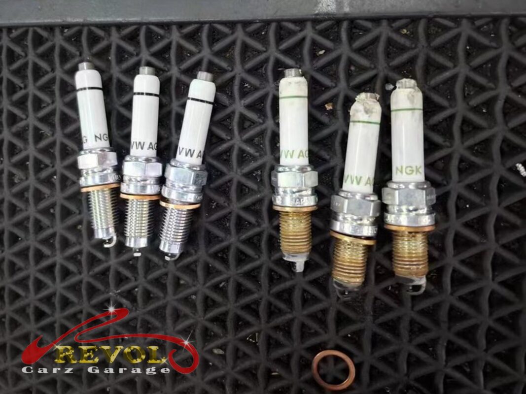 The three old spark plugs (right, threads discoloured) next to three fresh ones (left), with a new sump drain washer below.