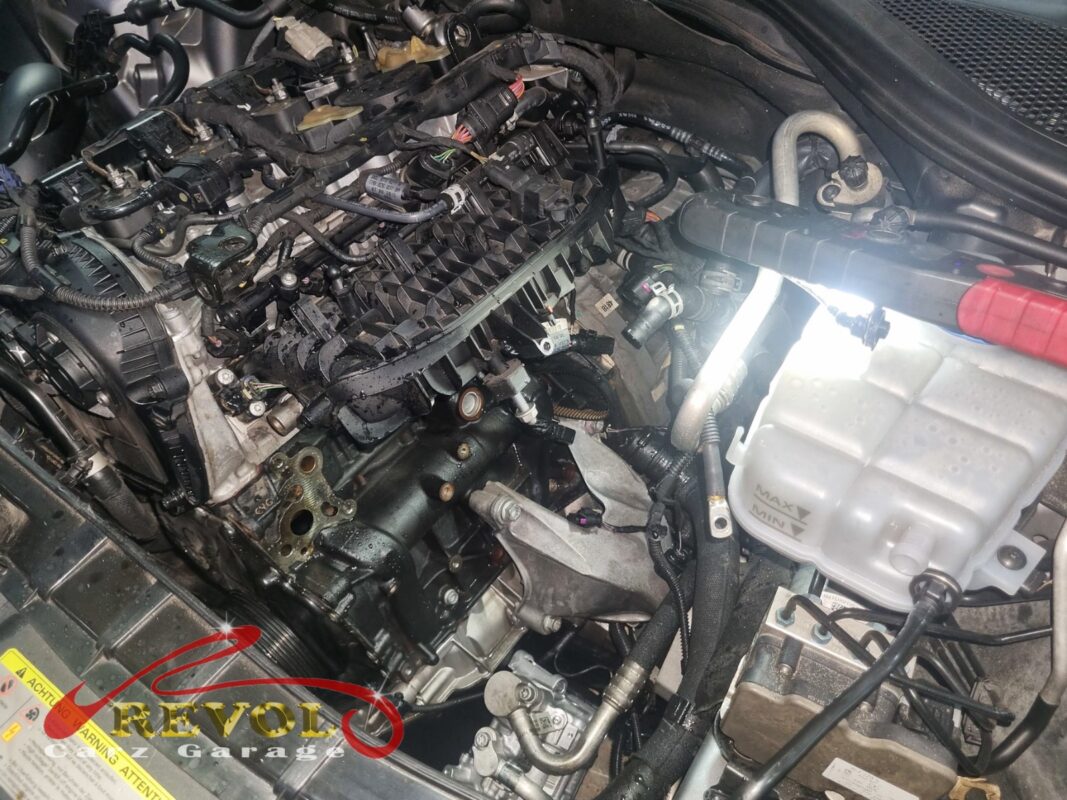 The engine partly stripped around the thermostat housing, the coolant expansion tank to the right.