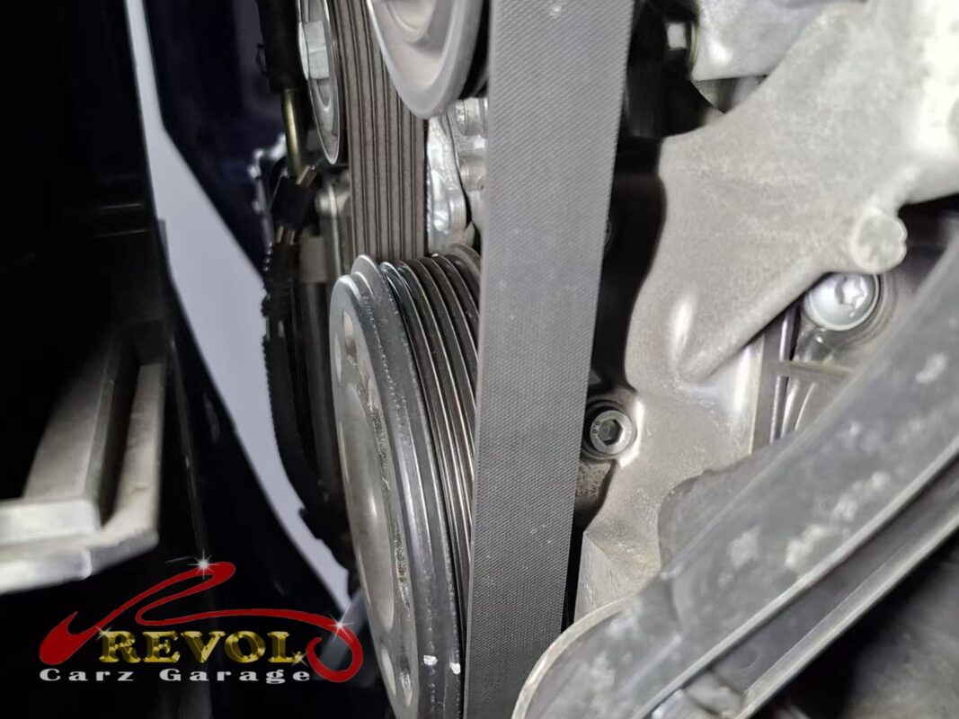 The auxiliary belt running over the crankshaft, tensioner and alternator pulleys, glazed along the rib face after 120,000 km.