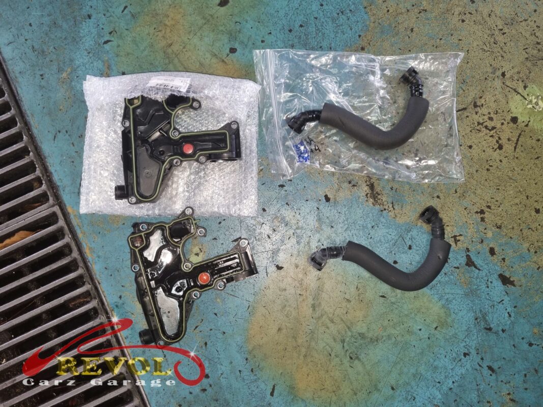 The old oil-gas separator (lower left, grimy) next to the new VAG-spec replacement (upper left, still bagged), with a fresh breather hose and clamps alongside.