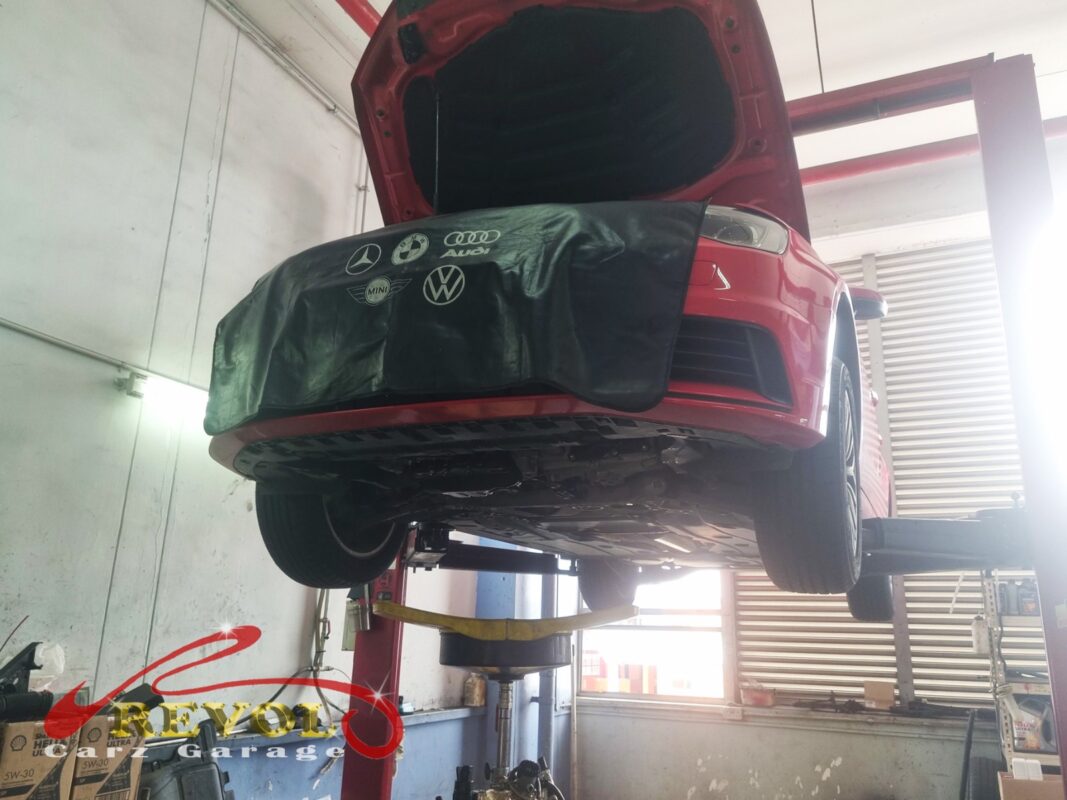 The red Audi A3 up on the two-post lift, fender cover on, in for the rear suspension work.