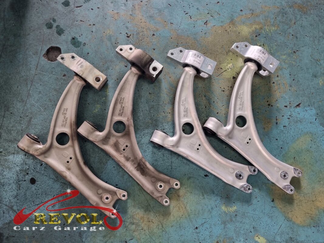 The two old front lower control arms (left, grimy with the torn bush still in place) next to the two new Audi-spec replacements (right).