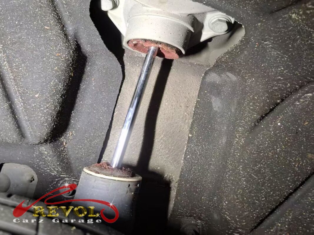 A rear shock absorber still on the car, the top mount rubber breaking down and the body showing its age.