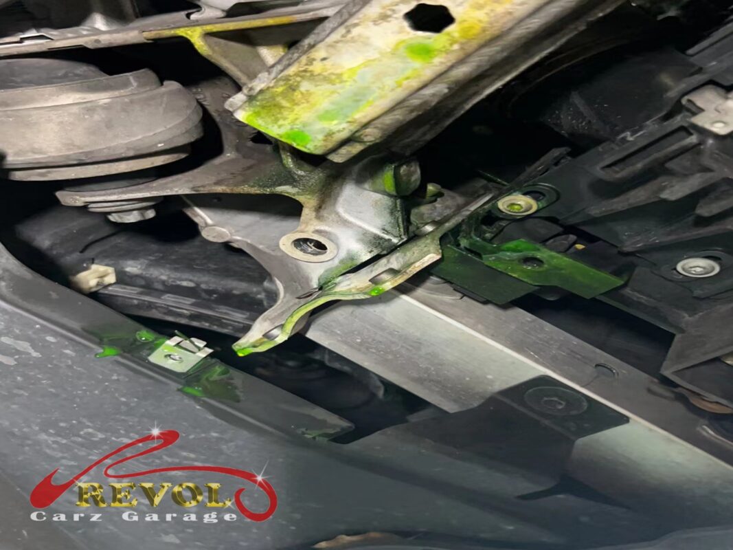 Bright green coolant residue splashed across the radiator support and crossmember, the trail of a leaking radiator.