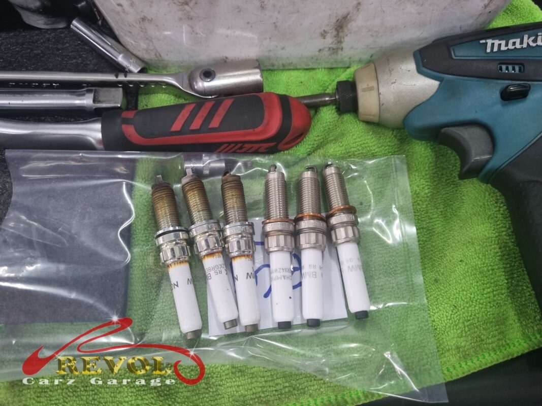 The old spark plugs (left, threads discoloured) next to fresh BMW-spec replacements (right), pulled for inspection and renewed.