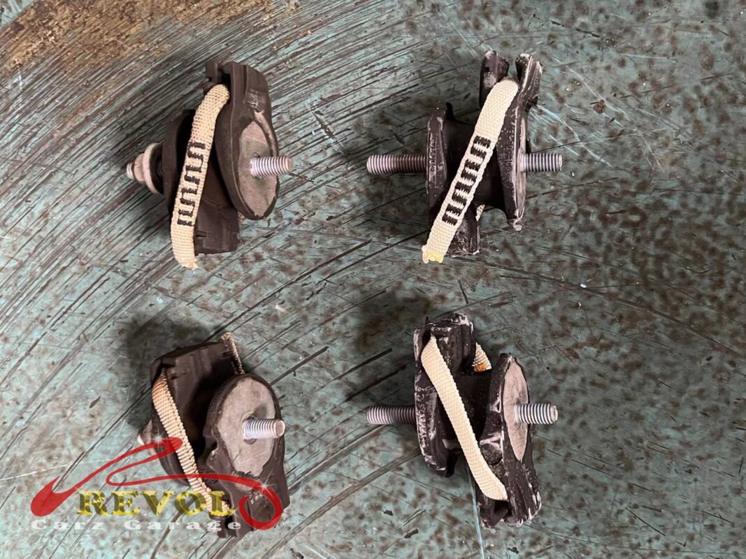 Gearbox mounts laid out, the cloth heat-shield strap wrapped around each, the old set out and new BMW-spec ones in.