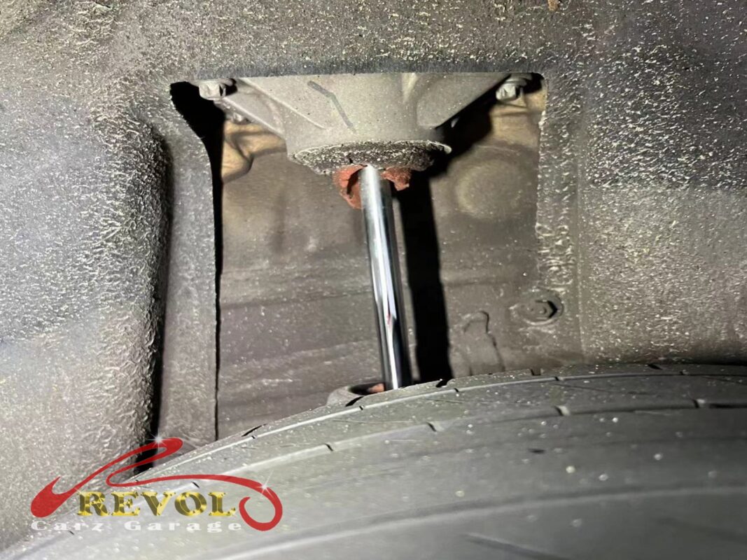 A rear shock absorber on the car, oil weeping down its body, the top mount rusty with age.