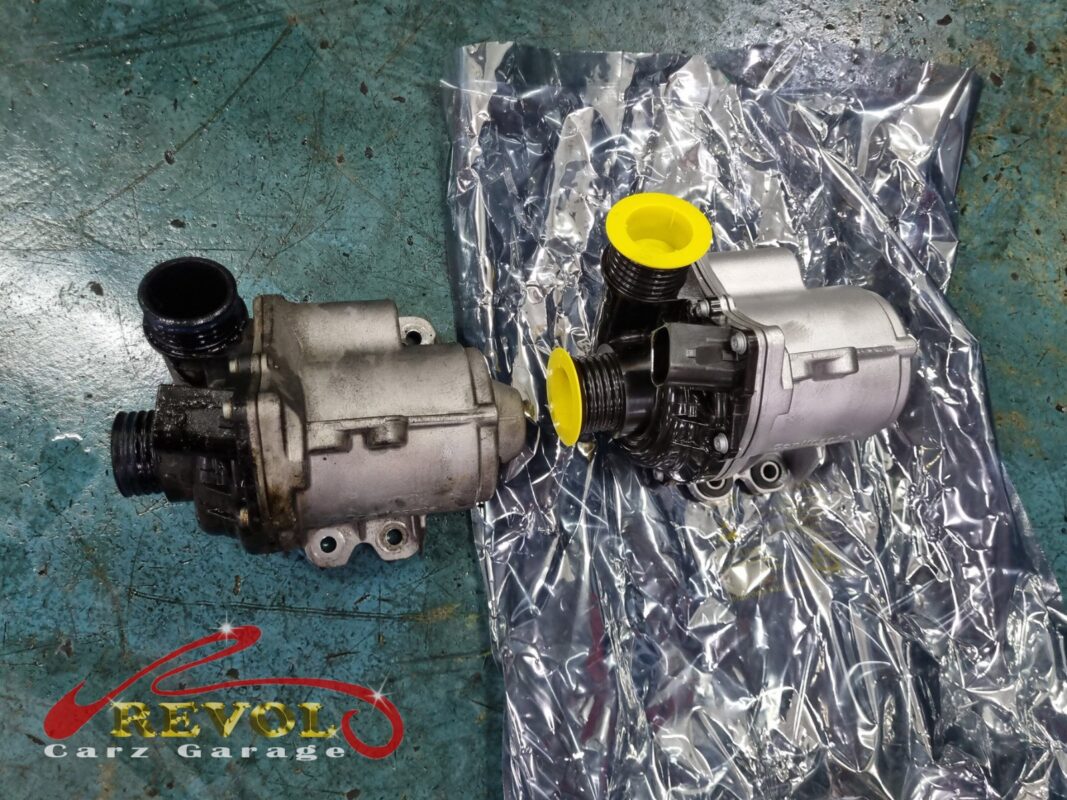 The old electric coolant pump (left, grimy) next to the new BMW-spec replacement (right, with the port caps still on).
