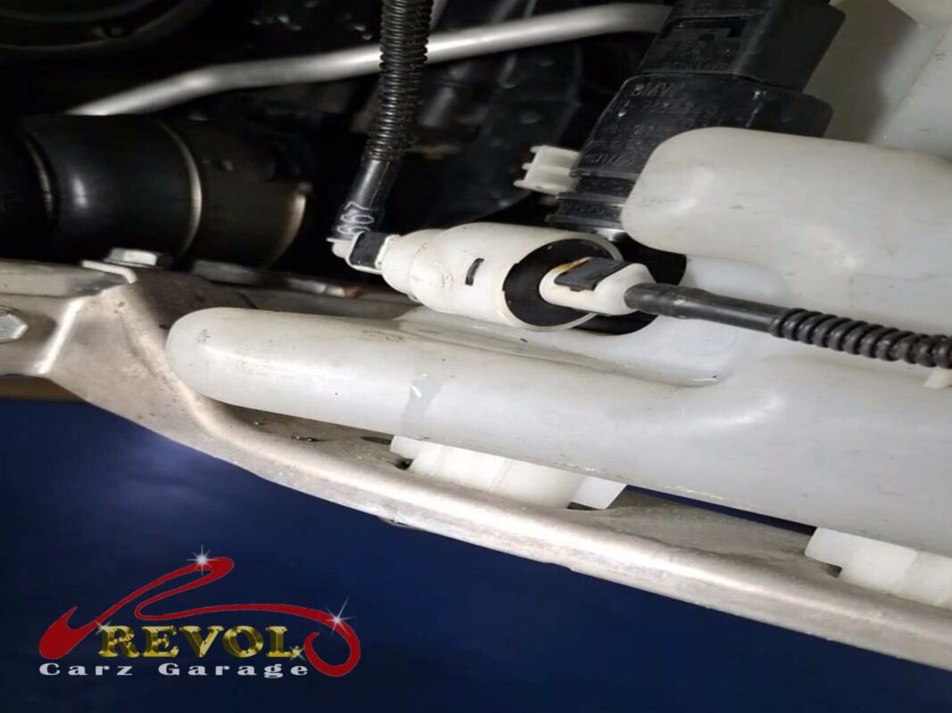 The washer fluid tank in the engine bay, the pump motor seated in its grommet with the supply hose and electrical plug connected.
