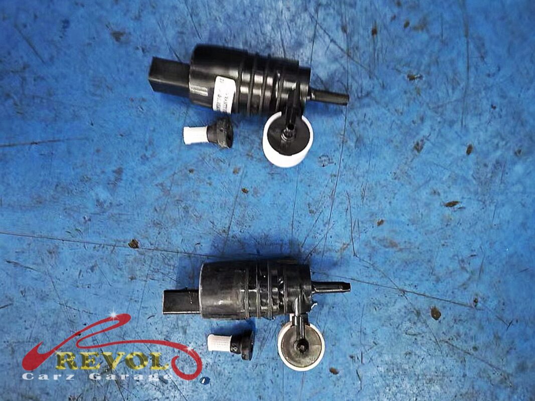 The old washer pump motor next to the new BMW-spec replacement, each with its white filter sock, the worn one no longer building pressure.