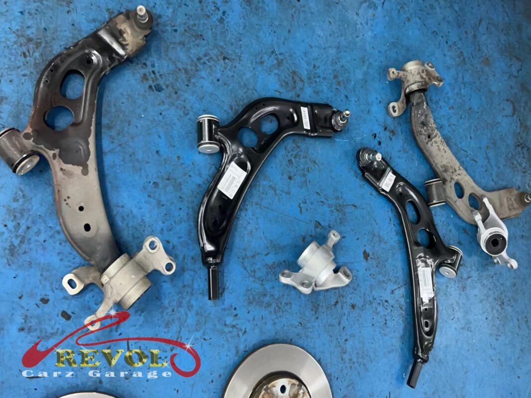 The two old lower control arms (left and top right), worn and rusted, beside the new BMW-spec replacements with their fresh bushes.
