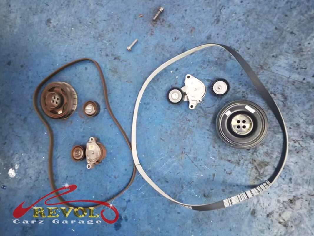 The old parts off the engine: the ribbed accessory belt, its tensioner and idler pulleys, and the crankshaft pulley, the worn pieces behind the rattle.