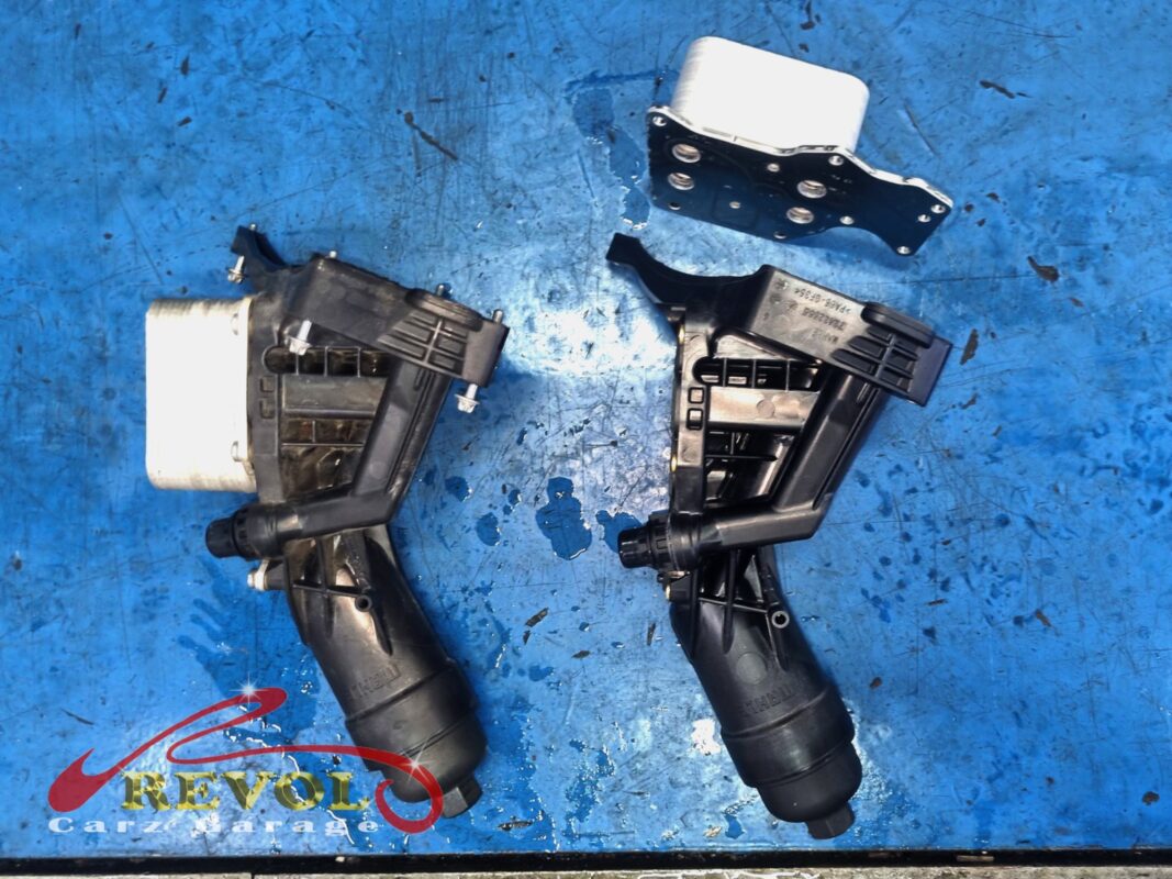 The old oil filter housing module (left, grimy) beside the new BMW-spec replacement and its oil cooler (right).