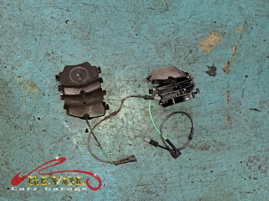 The worn front brake pads with their sensor wires (right) beside the new set (left), due at this service.