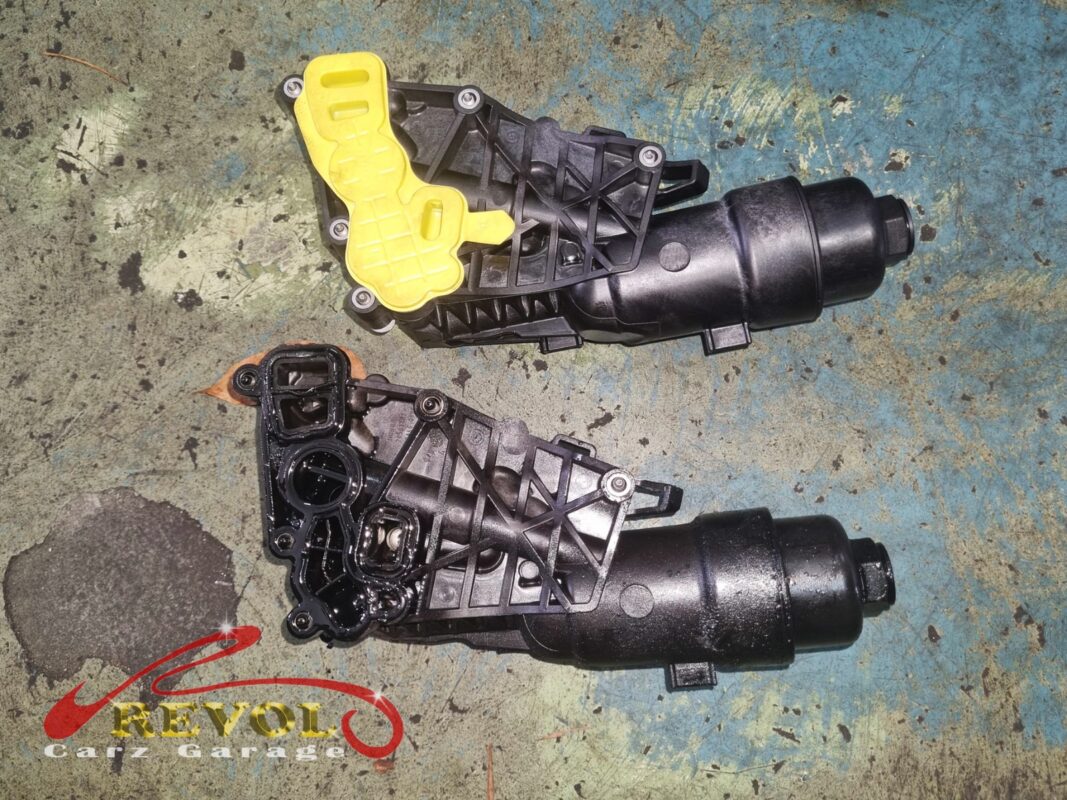 The old oil filter housing (bottom, oil-stained) beside the new BMW-spec replacement (top).
