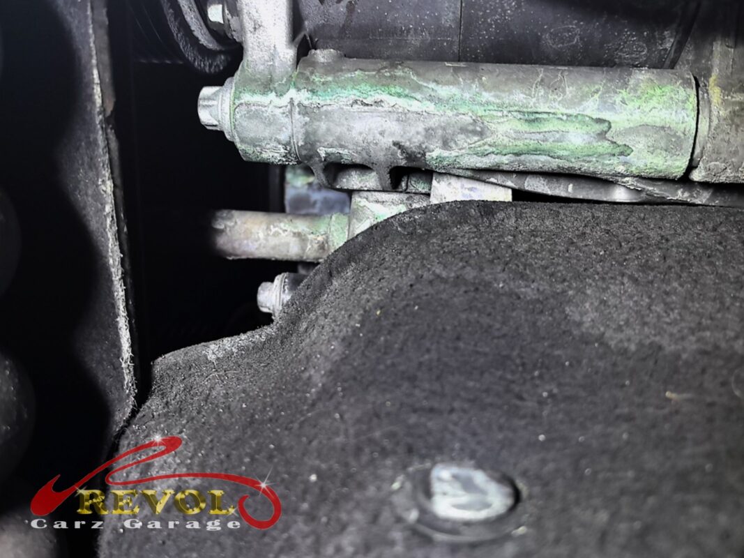 Green crusty residue from leaking coolant baked onto the pipework around the water pump, the leak made visible.