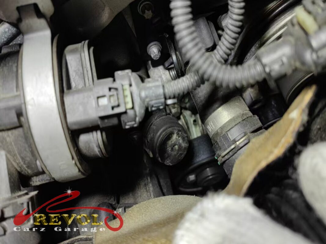 The water pump area in the engine bay, faint coolant residue around the connections.