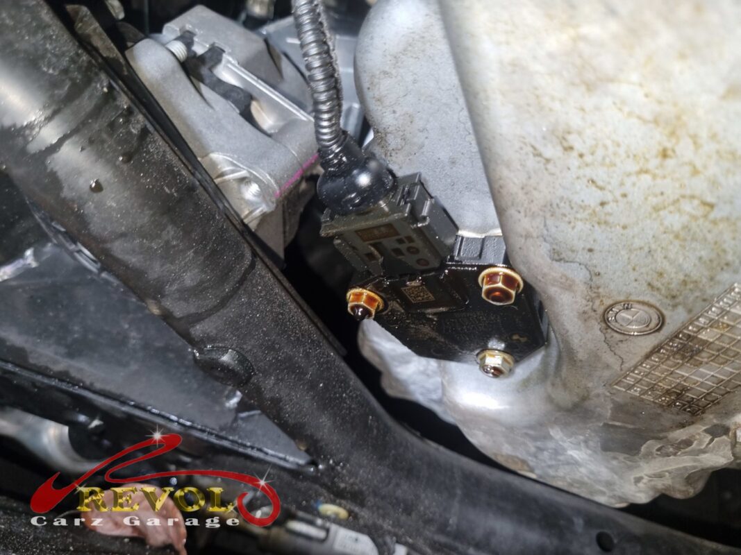 The oil level sensor in the bottom of the sump, the area around it oil-stained from a weep at the housing.