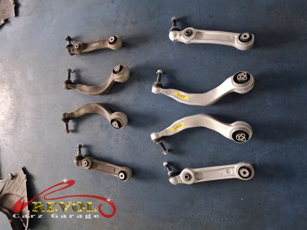 The full set of front control arms laid out, the worn arms beside the new BMW-spec replacements.