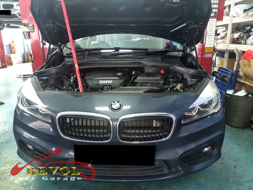 BMW 216d with the engine cover off and the timing pulley exposed for replacement.