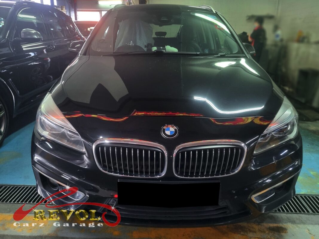 BMW 216d on the workshop lift with both front wheels off for control arm replacement.