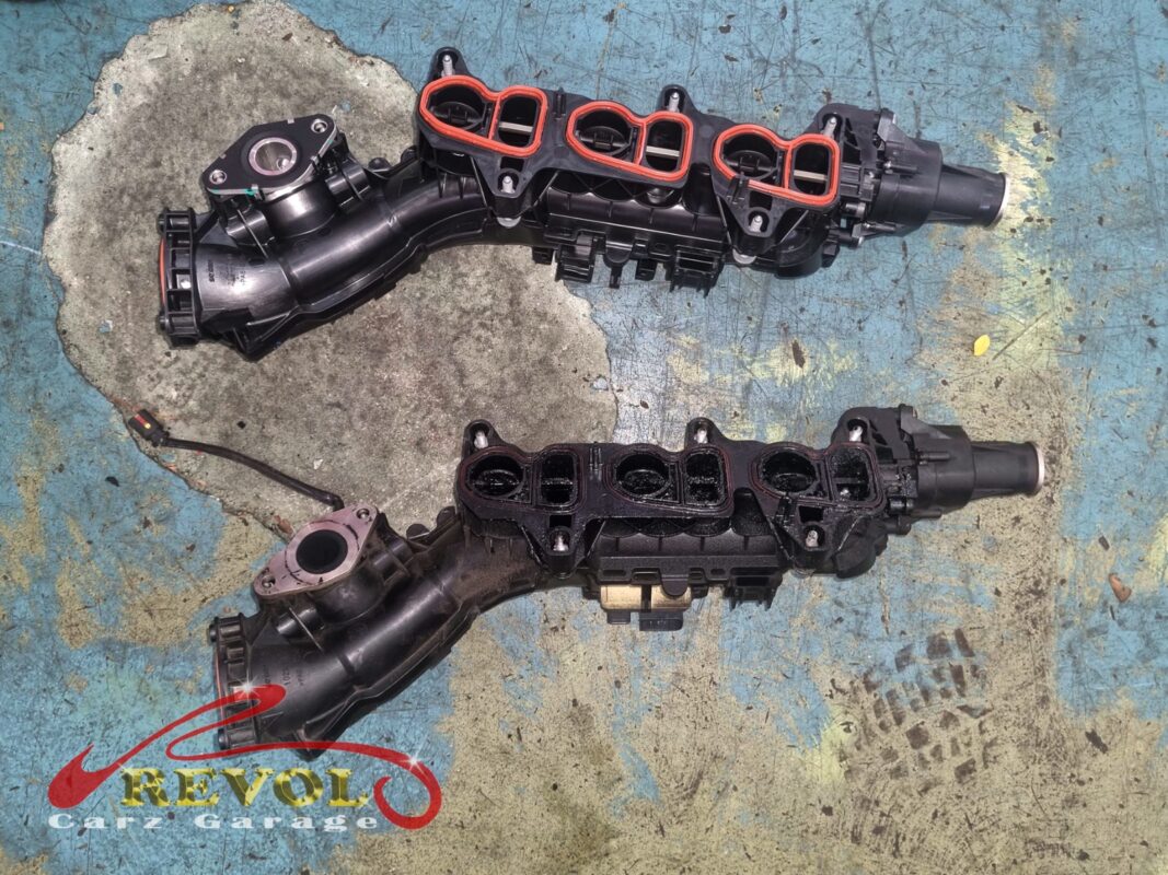 The old intake manifold (bottom, oily) beside the new BMW-spec replacement with its gaskets and actuator (top).