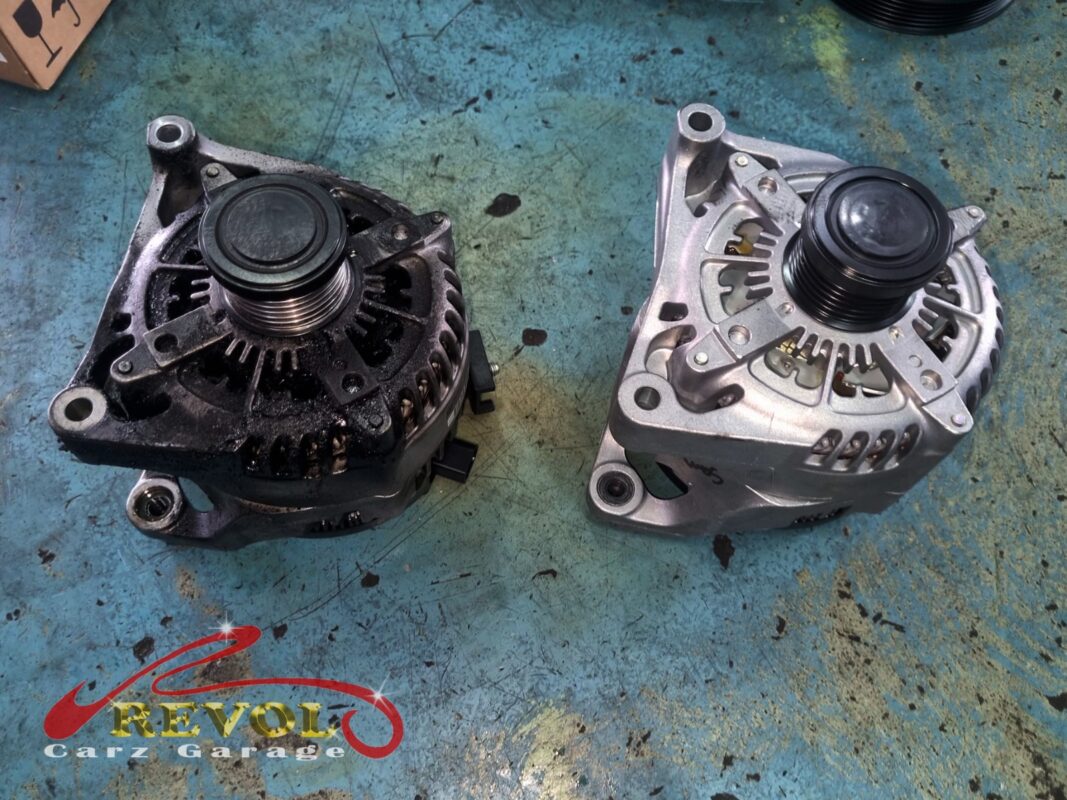 The old alternator (left, grimy) beside the new BMW-spec replacement (right), the sunken overrunning pulley behind the slipping belt.