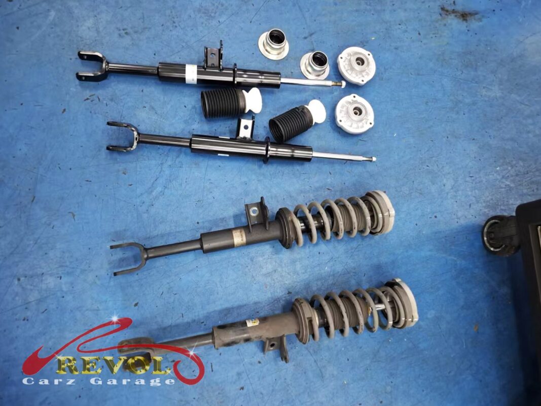 The new BMW-spec front struts with fresh top mounts and bump stops (top) beside the worn old strut assemblies (bottom).