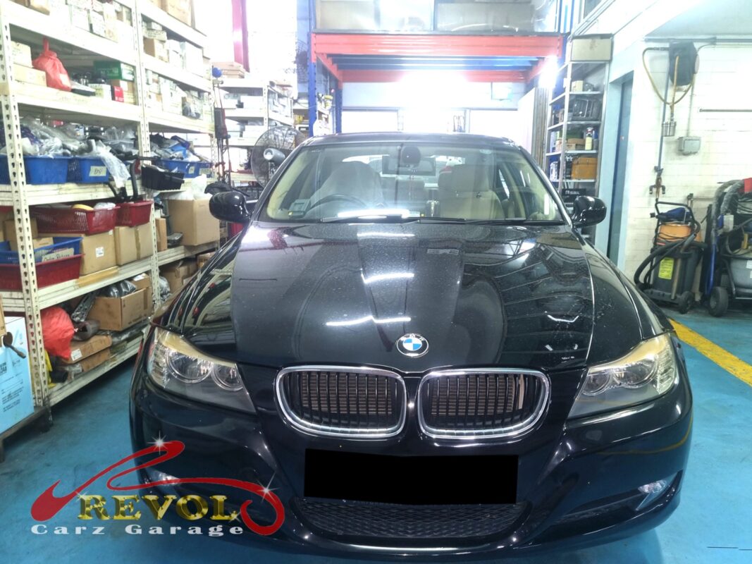 BMW 318i on the workshop lift with front wheels off for control arm replacement.
