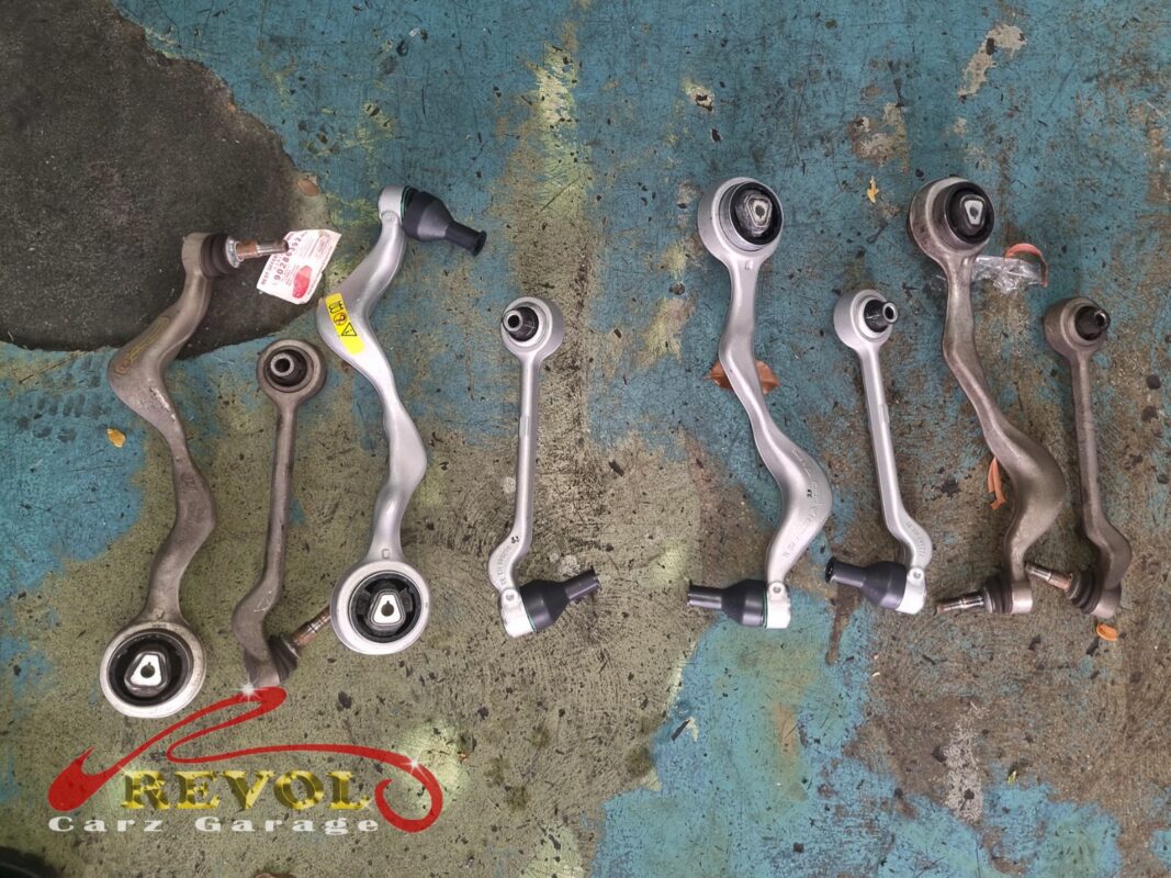 The full set of front control arms laid out, the worn arms beside the new BMW-spec replacements.
