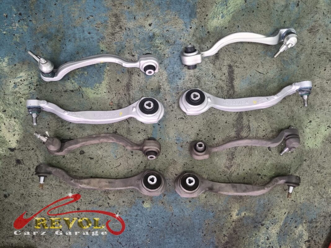 The full set of front control arms laid out, the worn arms beside the new Mercedes-spec replacements.