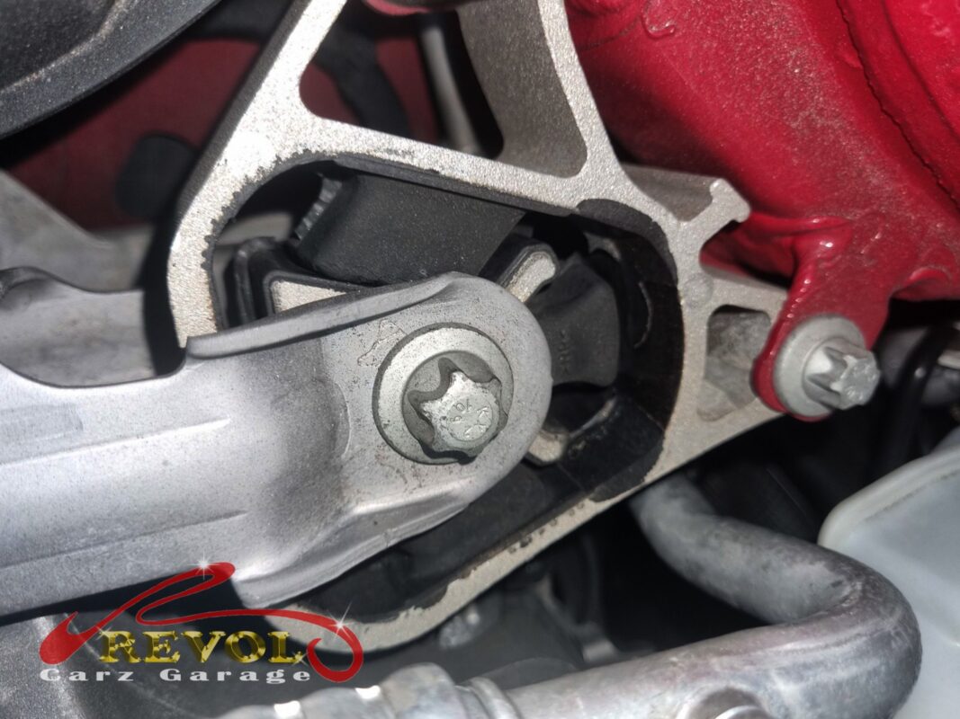 An engine mount on the car, the bracket and the worn rubber visible in the bay.