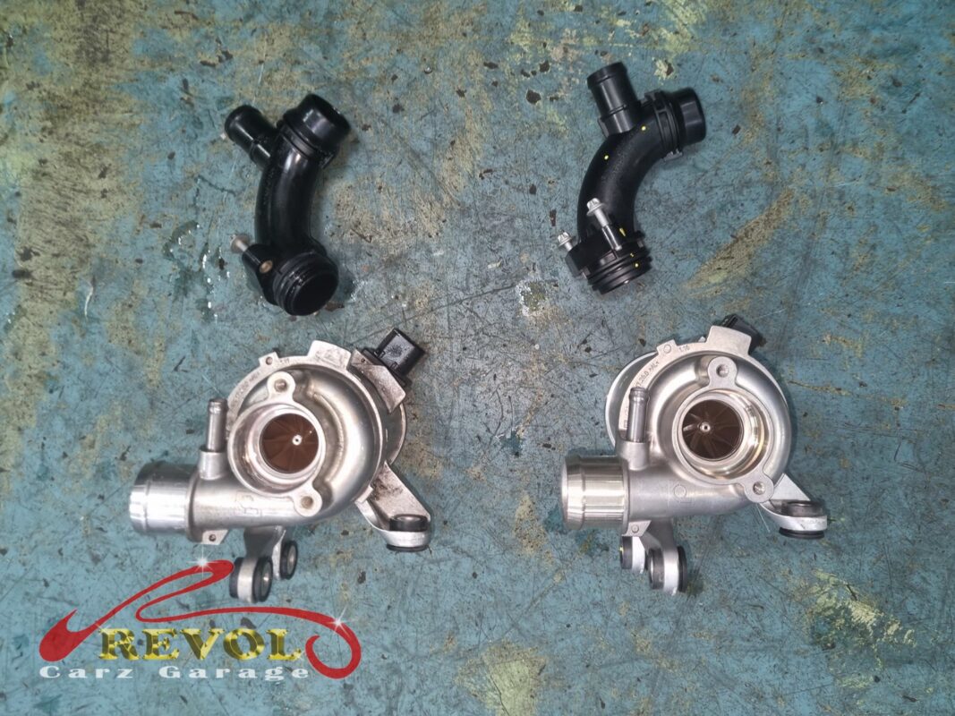 The old electric coolant pump and its connecting pipe beside the new Mercedes-spec replacement.