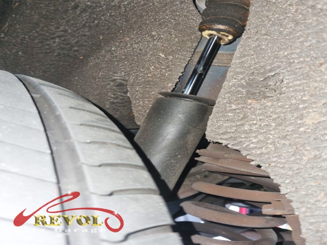 A rear shock absorber in place under the car, the corroded coil spring alongside it.