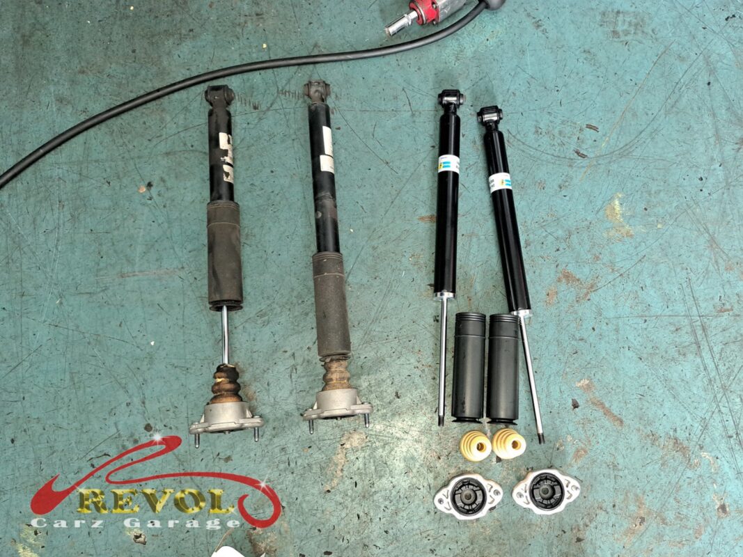 The two old rear struts (left, top mounts still attached) beside the new Bilstein pair (right) with fresh bump stops and mounts.