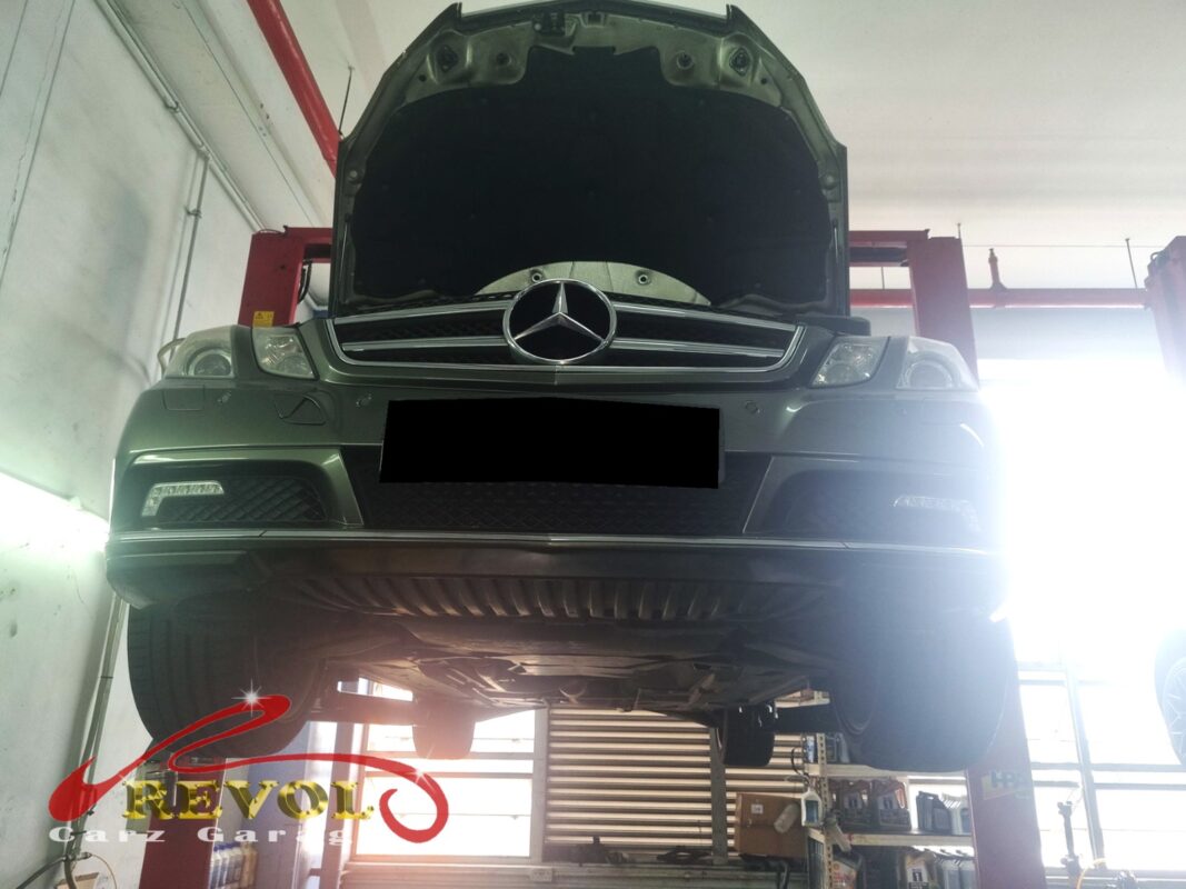The E250 up on the two-post lift, hood open, in for the suspension clunk.