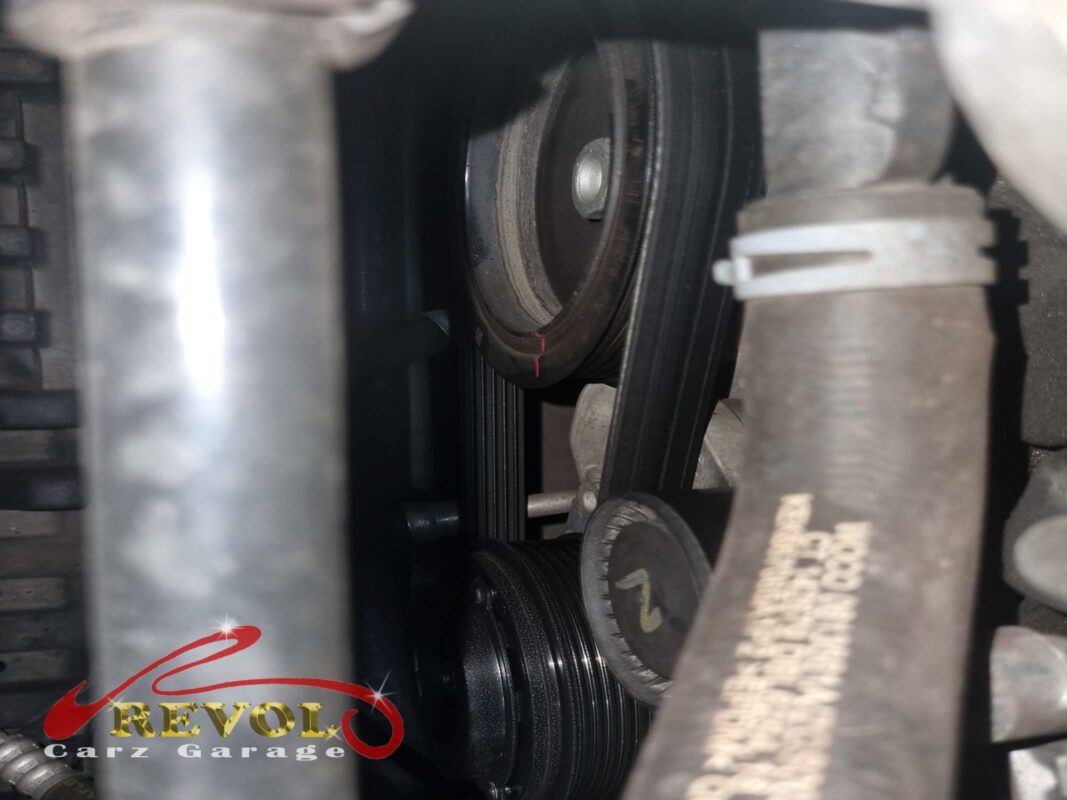 The accessory belt running over the drive pulleys at the front of the engine.