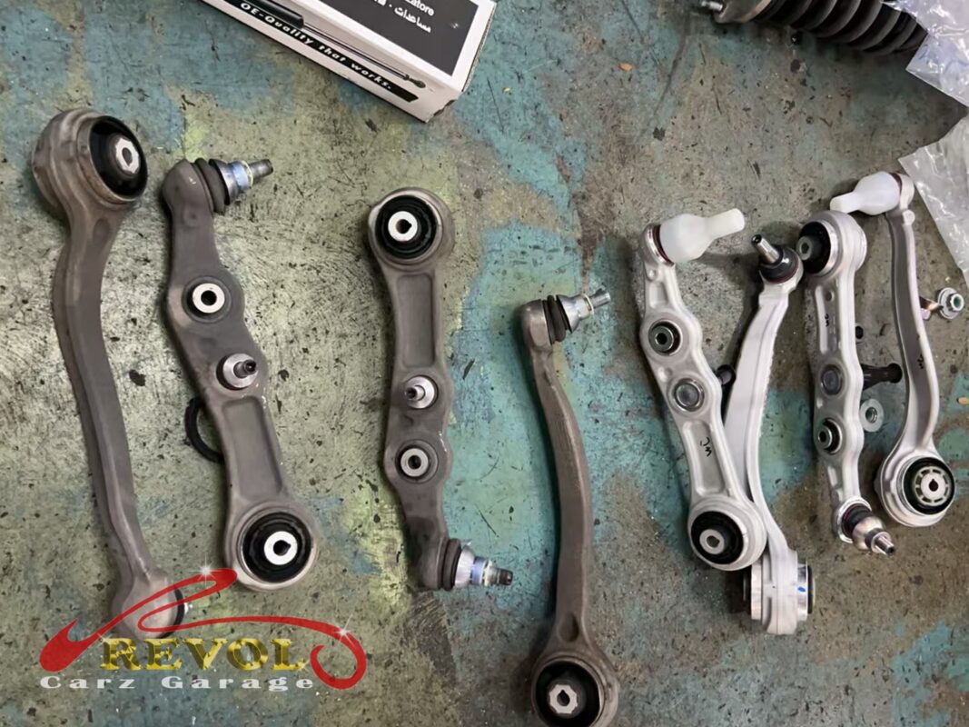 The old front control arms (left) beside the new Mercedes-spec set (right) with fresh bushes and ball joints.