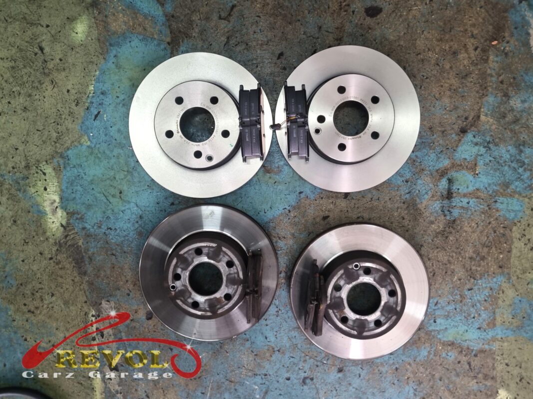The old brake discs and pads (bottom, worn with a lip on the edge) beside the new ones (top, fresh surface).