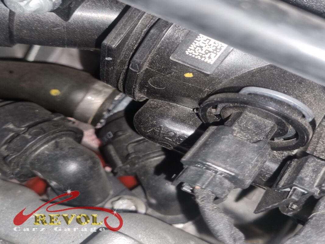 The thermostat housing in the engine bay, with its QR data label.