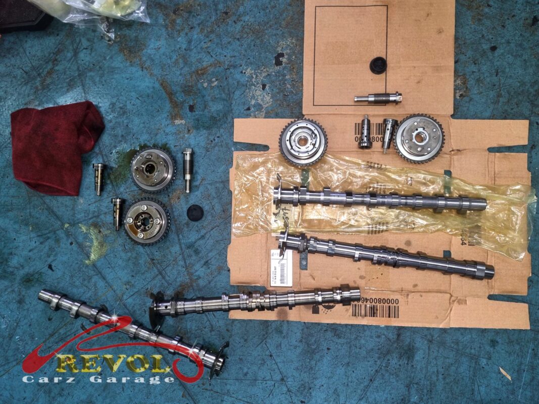 The new Mercedes-spec camshafts and adjusters laid out beside the old camshaft and parts removed.
