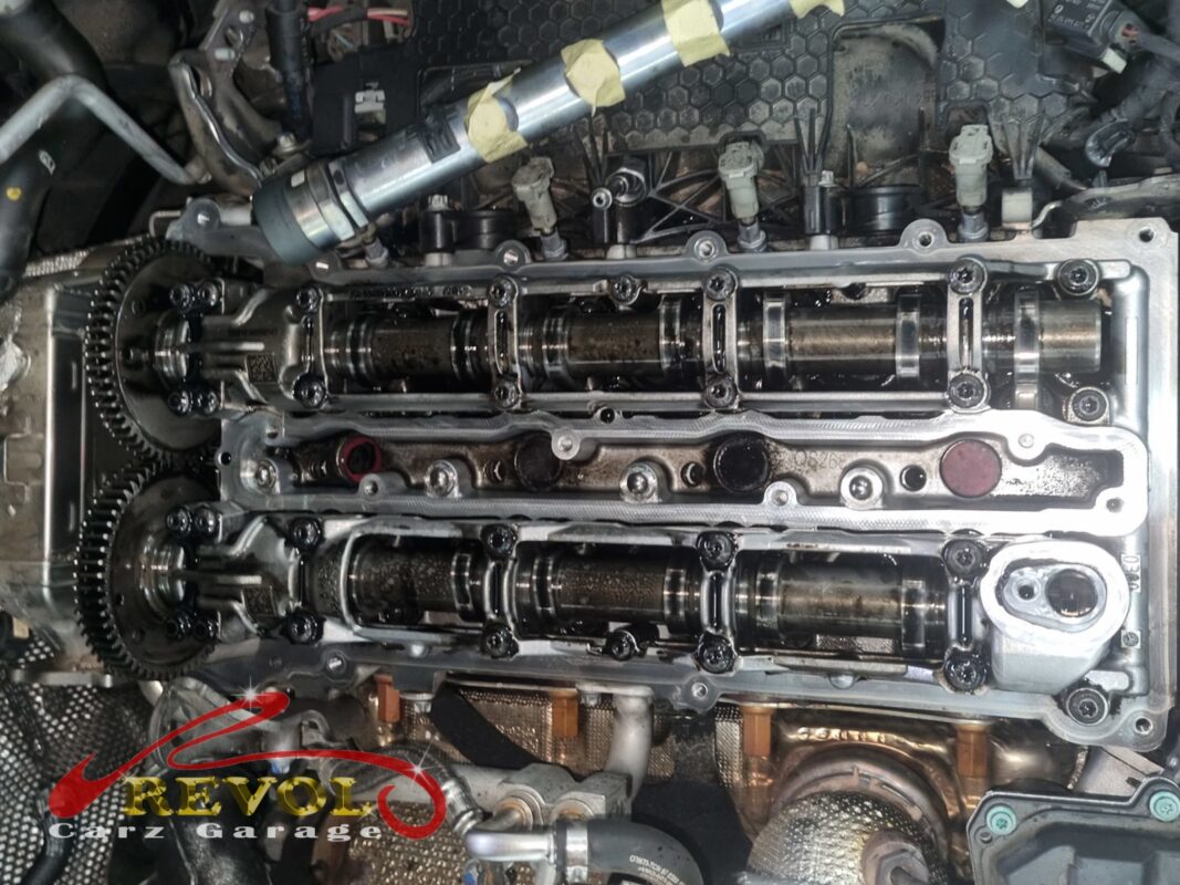 The cam cover off, the camshafts exposed and oil pooled across the head.