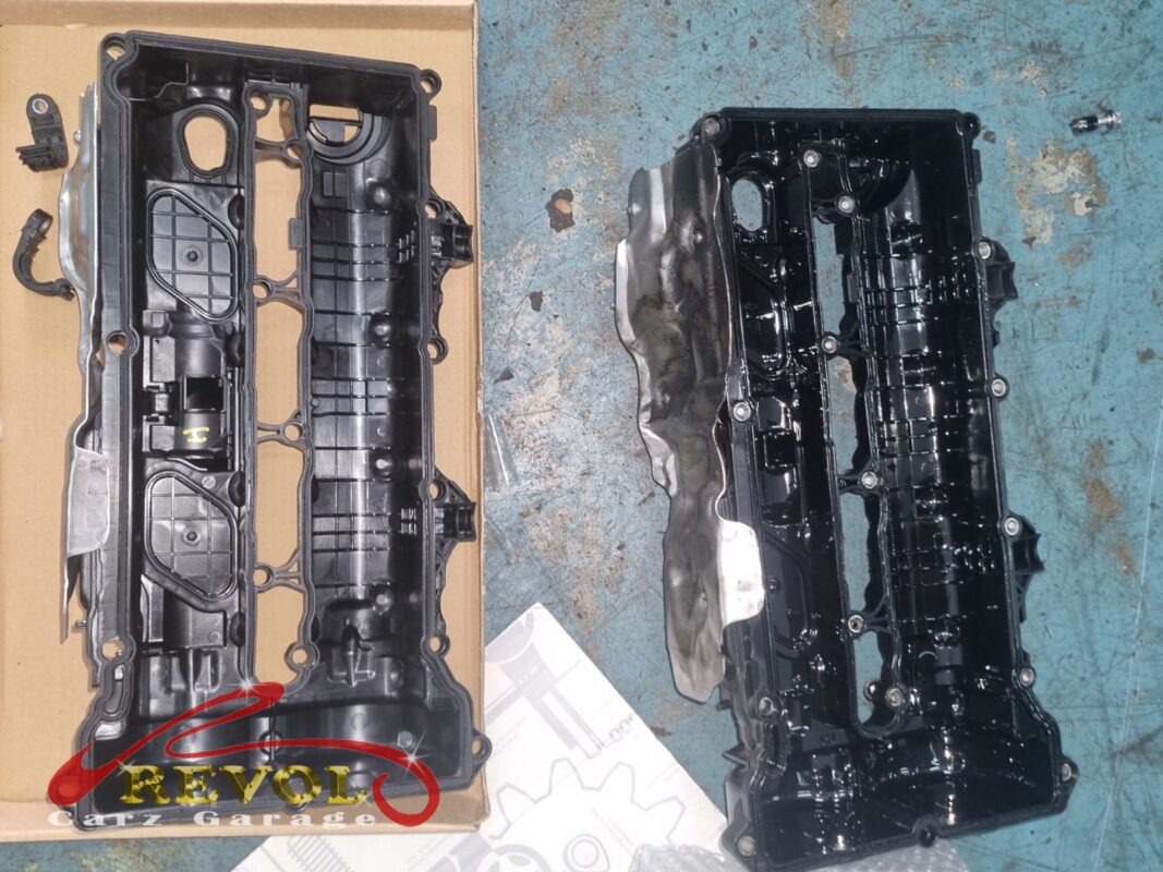 The old valve cover (right, underside oily) beside the new Mercedes-spec replacement (left, in its box).