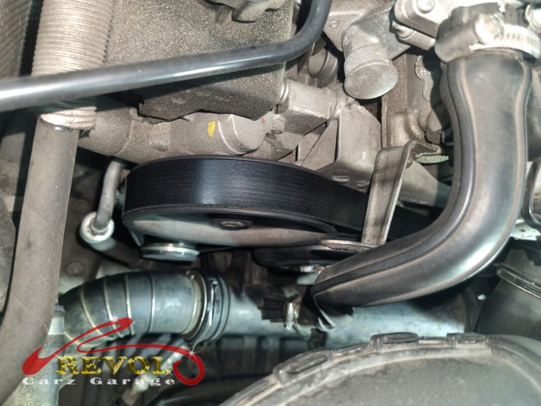 The accessory belt on the engine, running over the tensioner and idler pulleys.