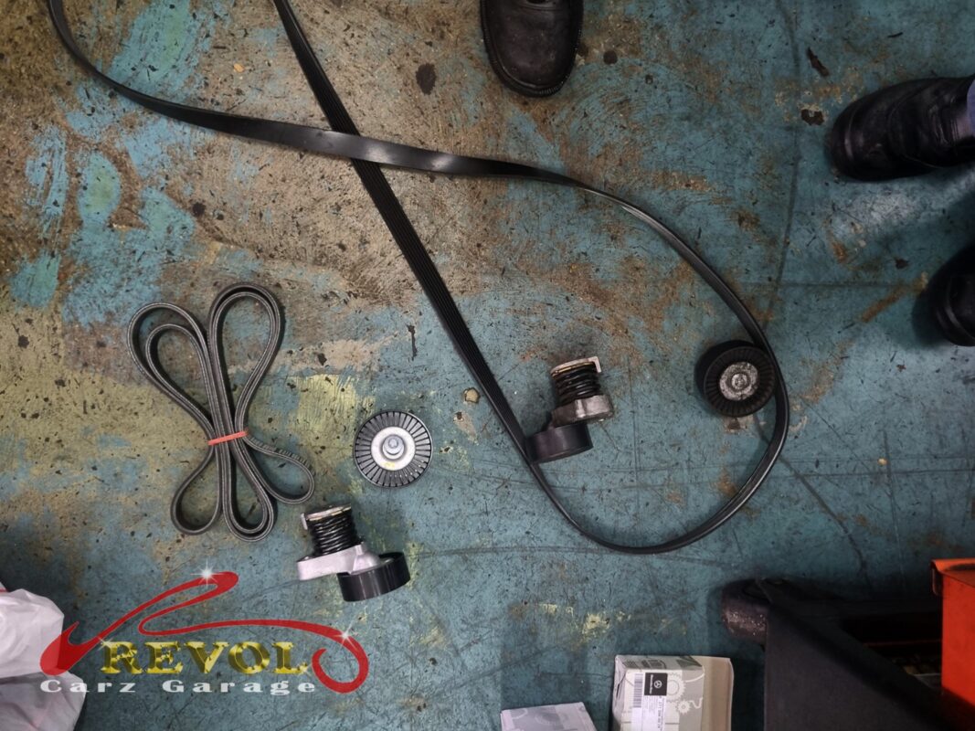 The old fan belt and tensioner beside the new Mercedes-spec belt, tensioner and idler.