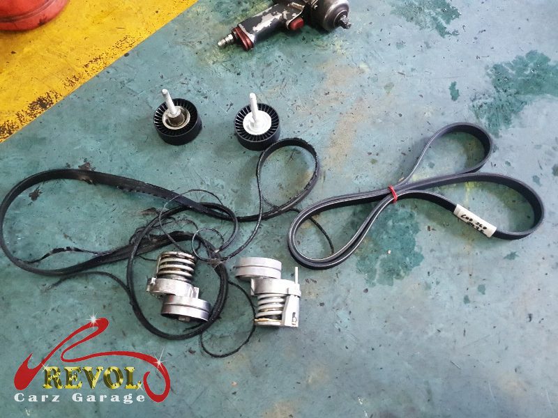 The old tensioner and idler pulleys removed alongside the belt.