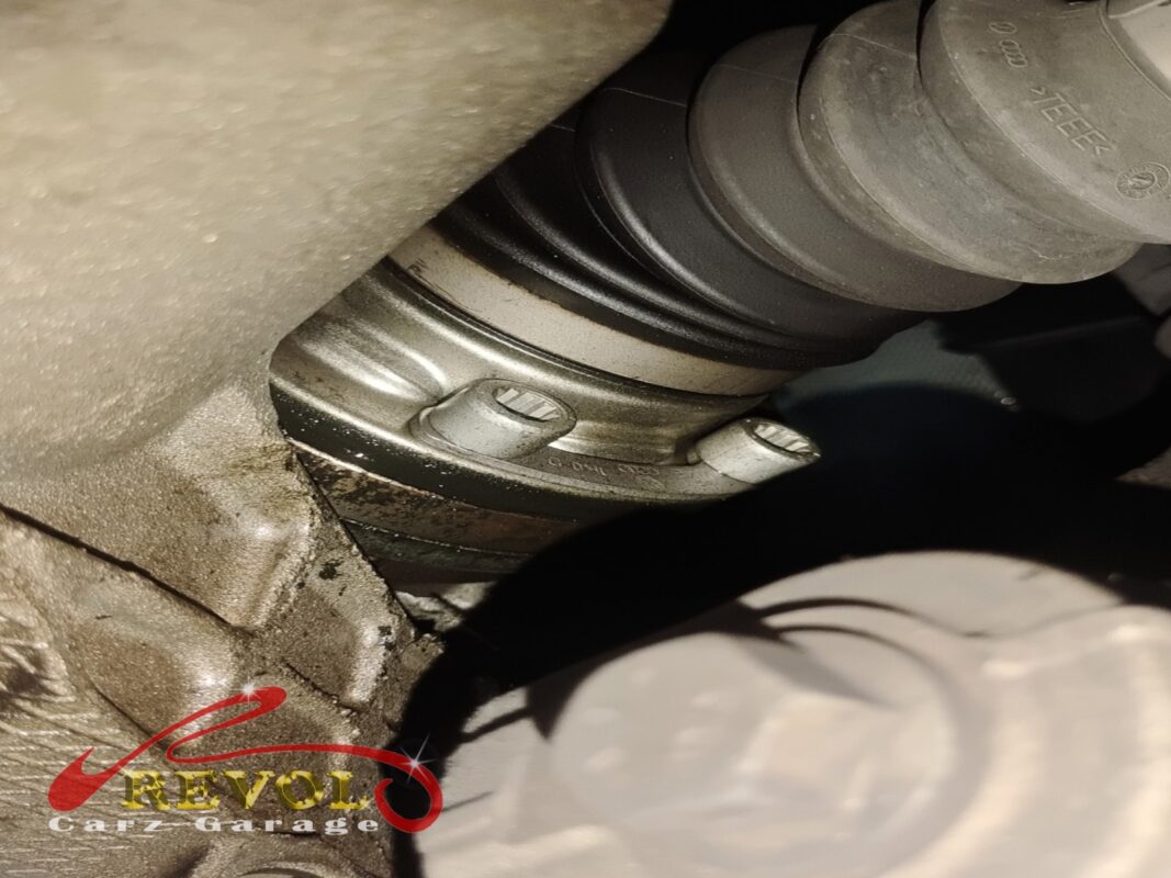 The inner driveshaft joint and its boot under the car, grime and grease around the housing.